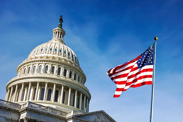  The United States Capitol and an American flag sits under a clear blue sky. 
